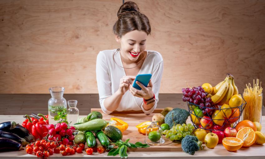 donna guarda telefono con intelligenza artificiale appoggiata ad un tavolo con frutta e verdura