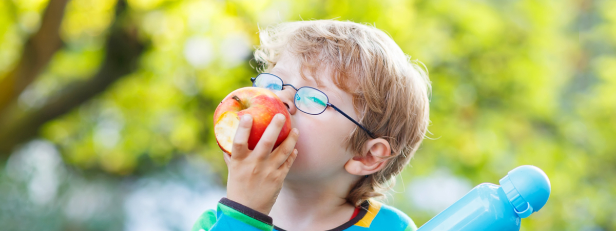 Bambino con occhiali che mangia una mela